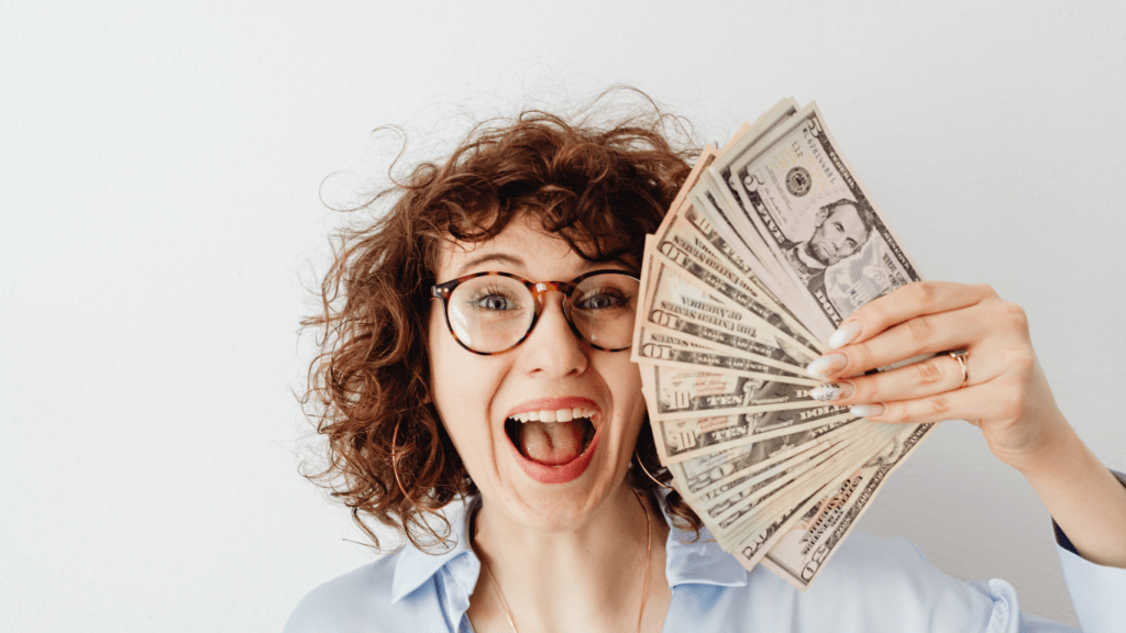 A person is holding a fan of money in front of their face