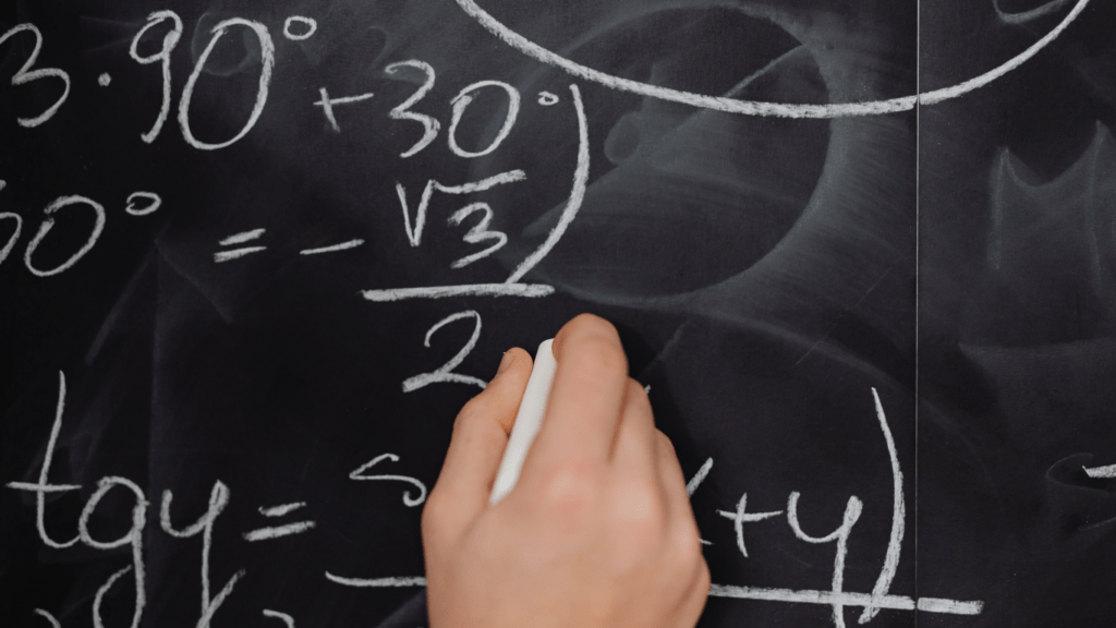 a person writing on a blackboard with formulas written on it