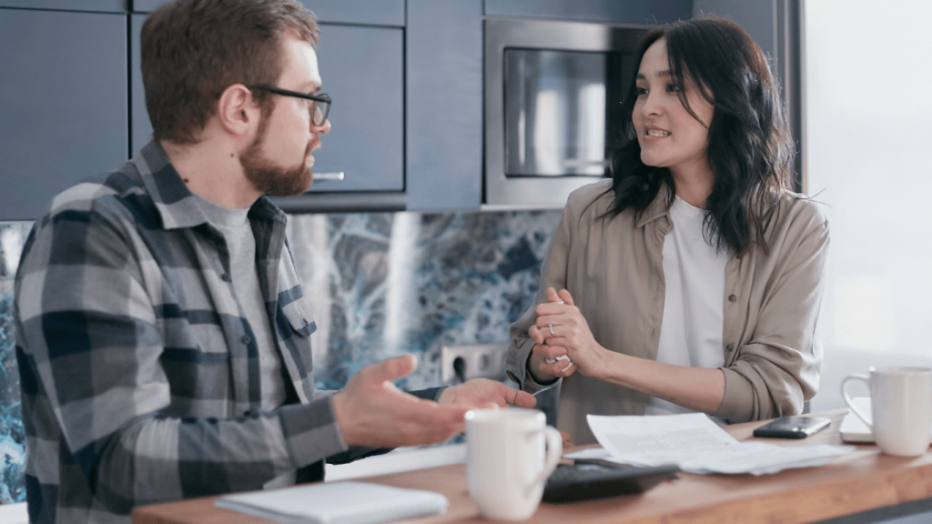 Two individuals sitting at a table talking and drinking coffee