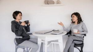 Two individuals sitting at a table talking and drinking coffee